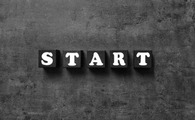 Koyu gri arkaplan üzerinde Başlat sözcüğünü taşıyan küpleri düz yatıyordu