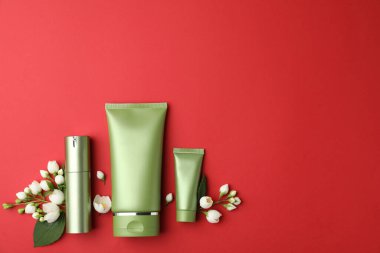 Kırmızı arka planda kozmetik ürünleri ve çiçekler var. Metin için boşluk