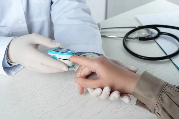 Stock image Doctor examining patient with fingertip pulse oximeter at white wooden table, closeup