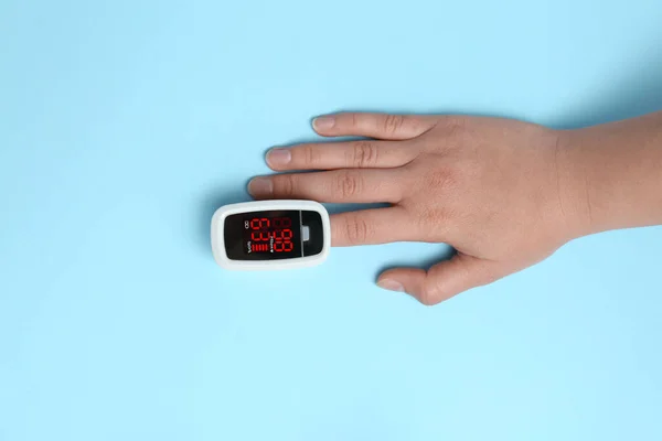 明るい青の背景に現代の指先パルス酸素濃度計を使用して女性 トップビュー — ストック写真