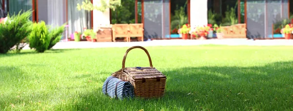 Picnic basket with blanket on green lawn in garden. Banner design