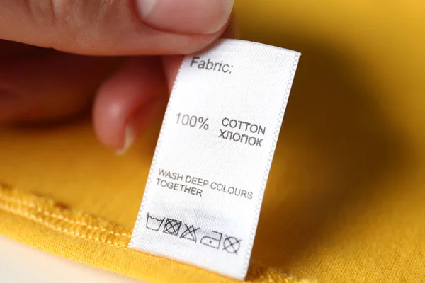 Kobieta Czytająca Etykietę Odzieży Symbolami Pielęgnacji Zawartością Materiału Żółtej Koszuli — Zdjęcie stockowe