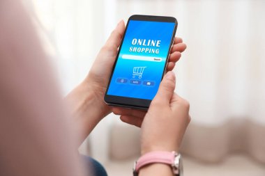 Çevrimiçi alışveriş sitesi olan akıllı telefonu elinde tutan kadın kapalı alanda, yakın plan