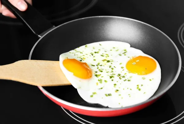 Woman cooking eggs in frying pan on stove, closeup