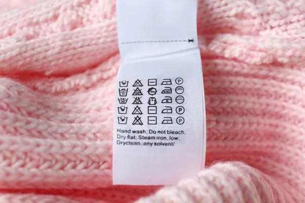Clothing label with care symbols on pink sweater, closeup view
