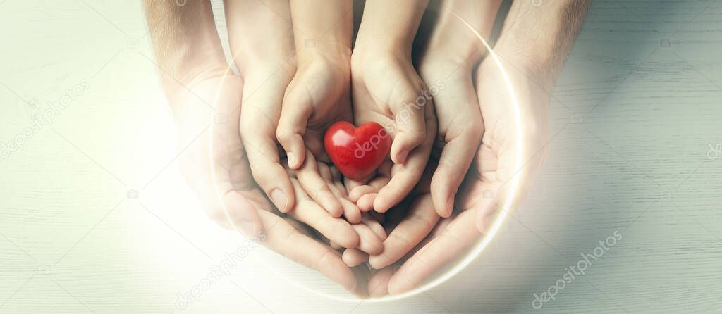 Family holding small red heart in hands on wooden background, top view. Banner design 