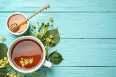Açık mavi ahşap masada çay ve ıhlamur çiçeğiyle bezenmiş düz bir kompozisyon. Metin için boşluk