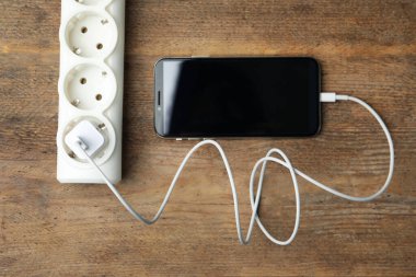 Akıllı telefon ahşap masada kabloyla şarj oluyor.