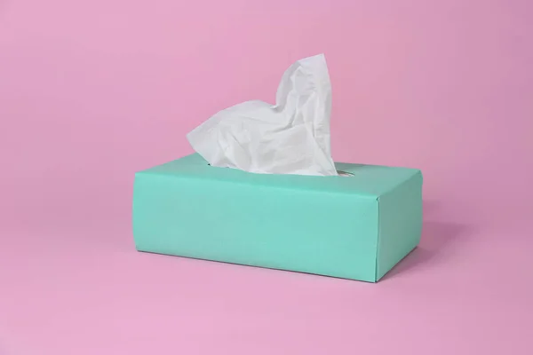 Box with paper tissues on pink background