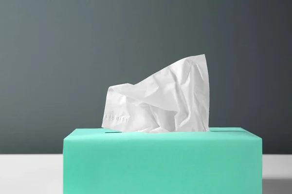 Box with paper tissues on table against black background, closeup