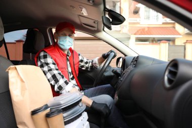 Koruyucu maskeli bir kurye ve arabada siparişleri olan eldivenler. Coronavirus karantinası sırasında yiyecek teslimatı