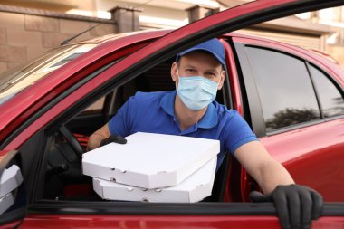 Koruyucu maskeli kurye ve pizza kutularıyla dışarı çıkan eldivenli. Coronavirus karantinası sırasında yiyecek teslimatı