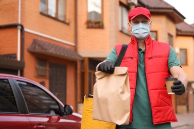 Koruyucu maskeli bir kurye ve dışarıda arabanın yanında siparişleri olan eldivenler. Coronavirus karantinası sırasında yiyecek teslimatı