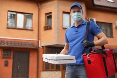 Koruyucu maskeli bir kurye ve evin yakınında pizza kutuları olan eldivenler. Coronavirus karantinası sırasında yiyecek teslimatı