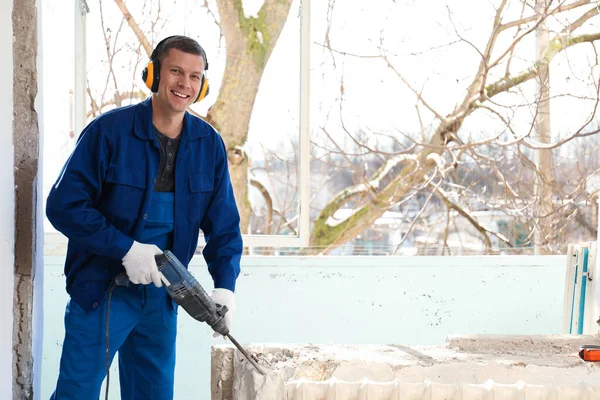Worker using rotary drill hammer for window installation indoors