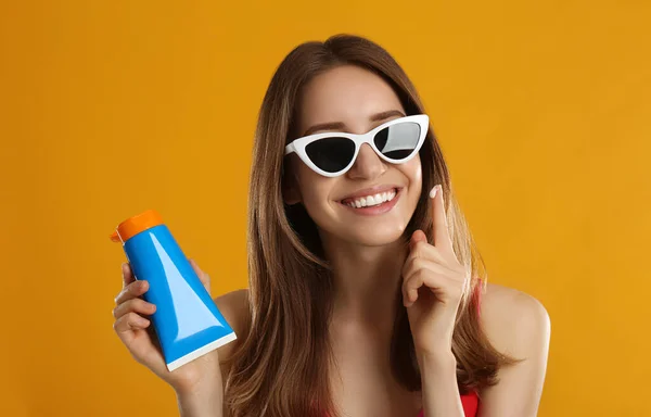Jonge Vrouw Die Zonnebrandcrème Oranje Achtergrond Aanbrengt — Stockfoto