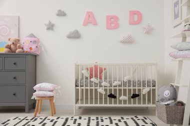 Beyaz duvarın yanında çekmeceleri ve beşiği olan şirin bir bebek odası.