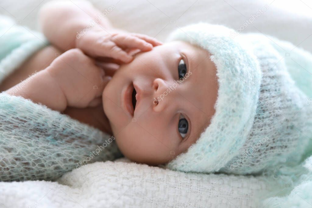 Cute newborn baby in warm hat lying on white plaid, closeup