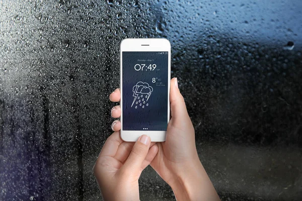 Woman using weather forecast app on smartphone near window indoors, closeup