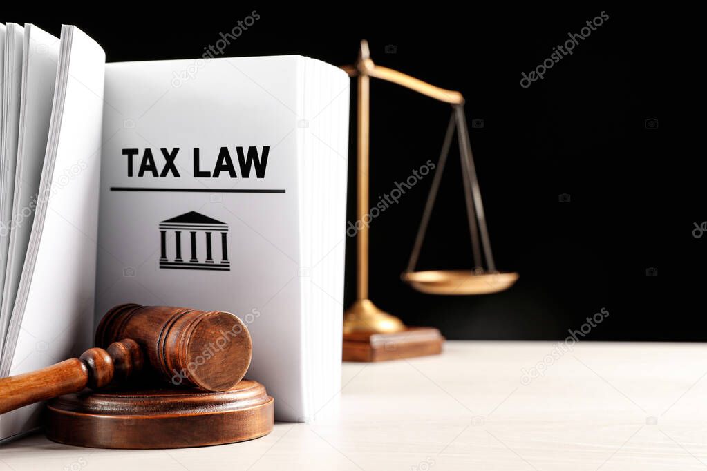 Tax law book, judge's gavel and scales on white table against black background. Space for text