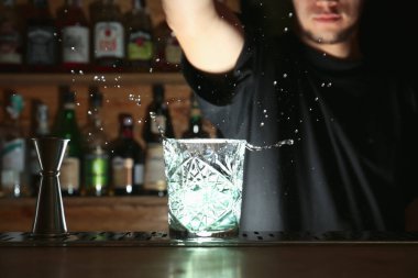 Barmen tezgahta taze alkol kokteyli hazırlıyor, cama odaklanıyor.