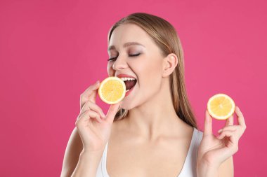 Pembe arka planda kesilmiş limonlu genç bir kadın. Vitamin zengini yiyecekler