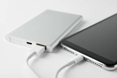 Beyaz arkaplanda elektrik bankasıyla çalışan akıllı telefon, yakın plan.