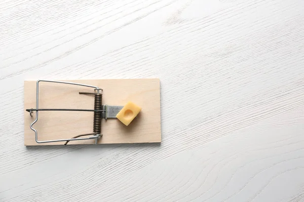 Mousetrap with piece of cheese and space for text on white wooden background, top view. Pest control