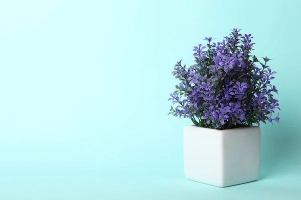 Artificial plant in flower pot on light blue background. Space for text