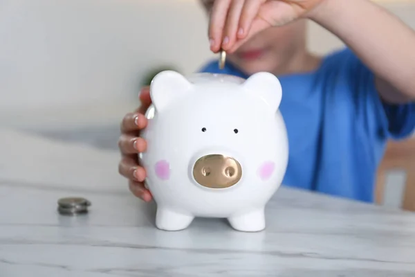 Little Boy Putting Coin Piggy Bank Marble Table Indoors Closeup — Stock Photo, Image