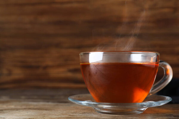 Cup of tasty black tea on wooden table. Space for text