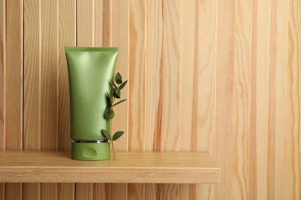 Tube of cosmetic product and plant on shelf near wooden wall, space for text