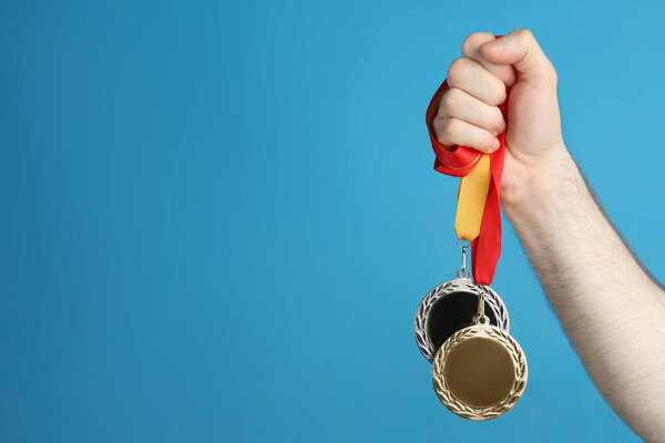 Man holding medals on blue background, closeup. Space for design