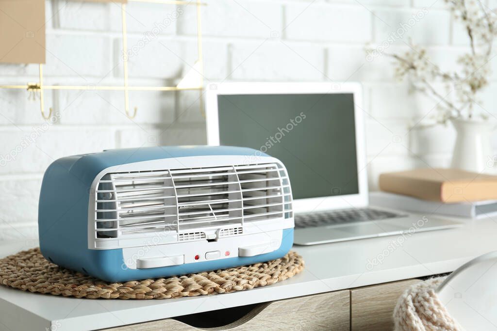 Modern air purifier near laptop on white wooden table in room