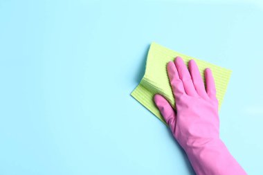 Açık mavi arka planda bez parçası olan kauçuk eldivenli biri, yakın plan. Metin için boşluk