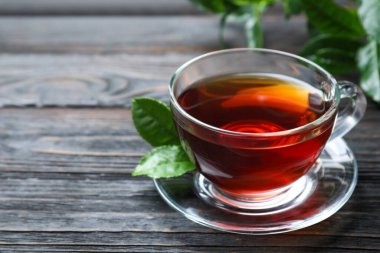 Cam bardak aromalı siyah çay ve ahşap masada yeşil yapraklar, metin için yer.