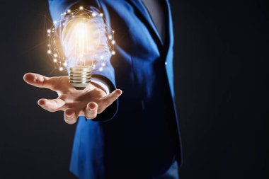 Fikir konsepti. Koyu arkaplanda parlayan ampulü olan bir iş adamı.