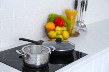Saucepot and frying pan on induction stove in kitchen clipart
