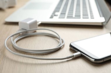 Akıllı telefon ve USB şarj aleti ahşap masada, yakın plan. Modern teknoloji