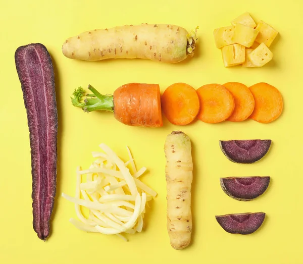 Whole and cut raw color carrots on yellow background, flat lay