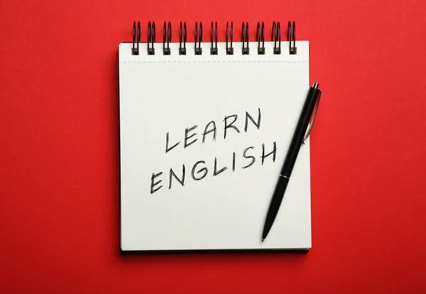带文字的开放笔记本学习英语和红色背景的钢笔 顶部视图 — 图库照片
