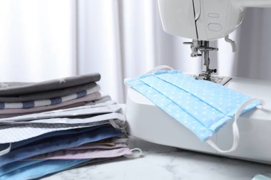 Dikiş makinesi ve beyaz mermer masada ev yapımı koruyucu maskeler.