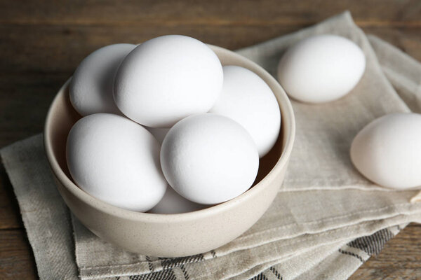 Many fresh raw chicken eggs in bowl on wooden table