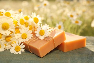 Sahadaki mavi ahşap masada sabun ve taze papatyalar.