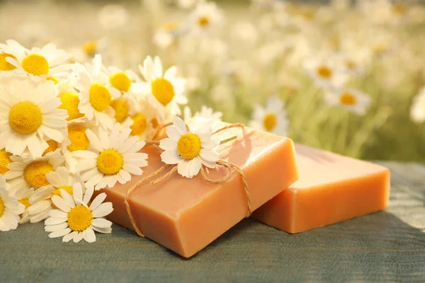 Sahadaki mavi ahşap masada sabun ve taze papatyalar.