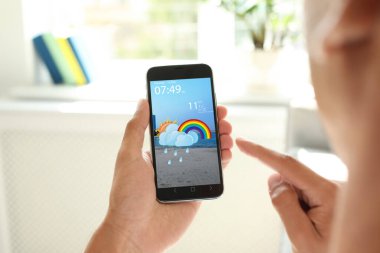 İçerideki akıllı telefondan hava tahmini uygulaması kullanan adam, yakın plan.