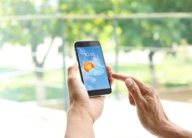 Pencerenin yanındaki akıllı telefondan hava tahmini uygulaması kullanan adam, yakın plan