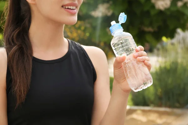 Young woman with bottle of pure water outdoors, closeup