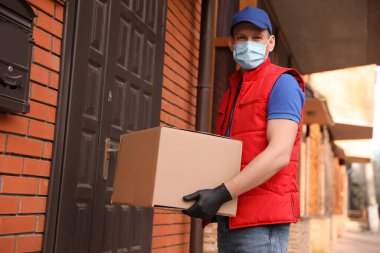 Koruyucu maskeli bir kurye ve evin girişinde kutusu olan eldivenler. Coronavirus karantinası sırasında teslimat servisi