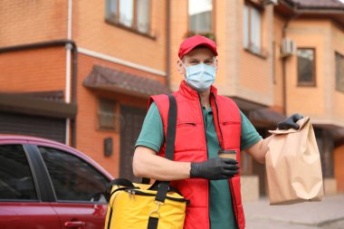 Koruyucu maskeli bir kurye ve dışarıda arabanın yanında siparişleri olan eldivenler. Coronavirus karantinası sırasında yiyecek teslimatı